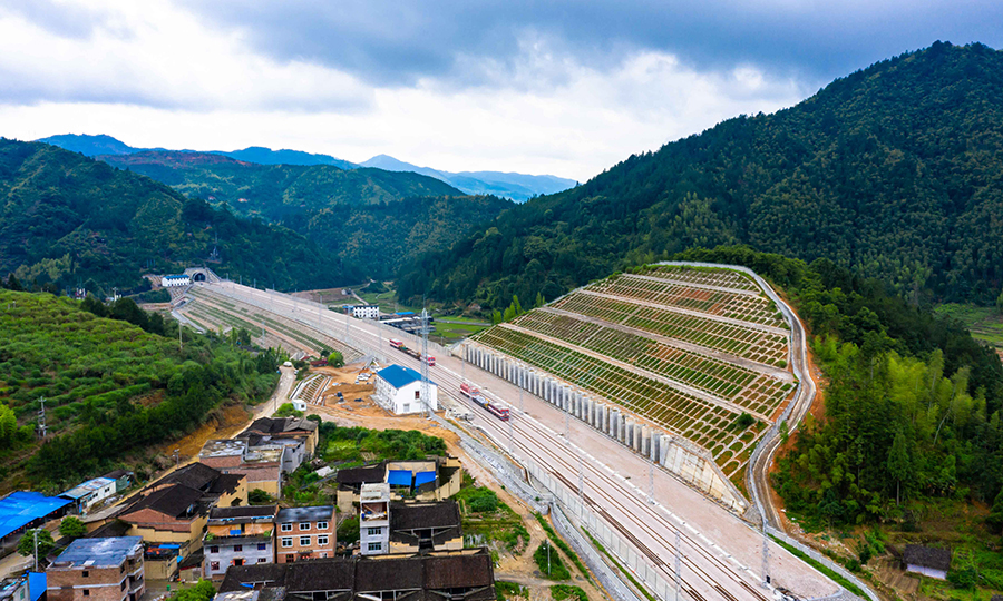 衢寧鐵路是一條典型山區鐵路。線路經過浙江省仙霞嶺、洞宮山及福建省鷲峰山三大山脈，全線高橋長隧工點較多，工程實施難度大。正線新建大中橋144座約51公里，新建隧道94座249公里，橋隧占比79%，全線猶如一條巨大的地鐵洞穿山岳。橋梁大跨特殊結構多、高墩橋梁較多，其中洋角大橋最大墩高達113米，相當于28層樓高；全線10公里長度以上隧道有7座，最長的鷲峰山二號隧道，全長17公里；高填深挖路基工點多，其中寧德北站為全線最高深路塹，九級邊坡，挖深達71米。圖為衢寧鐵路上墩（貨）站及遠處的全線最長隧道鷲峰山二號隧道。