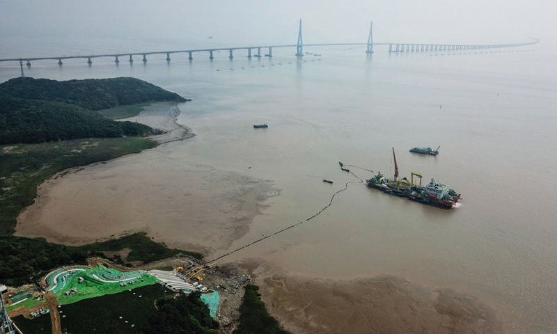 圖為6月2日，最后一段海底電纜從海纜施工船上緩緩?fù)舷蛑凵酱簌i山島的終端站，遠處是舟山跨海大橋。（新華社記者 徐昱 攝）