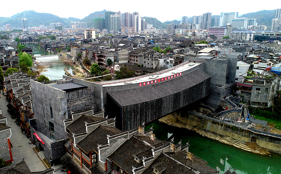 吉首美術館橋位于國家4A級景區(qū)湖南省吉首市乾州古城內(nèi)，橋梁總建筑面積約3500平方米。該橋采用“橋館合一”的設計理念，全橋由混凝土系桿拱橋及雙層鋼桁梁簡支梁橋兩座橋疊加組成，結構復雜，共包括3個部分：上層混凝土橋作為小型展覽廳，鋼桁梁頂部橋面作為大型展覽廳，鋼桁梁下層橋面為公共人行橋。這種上下兩個展廳和公共人行橋“三合一”的造型結構，屬亞洲首例。圖為美術館橋側景。