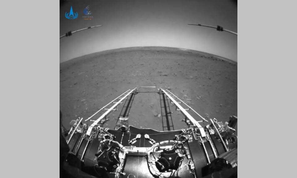 2021年5月19日，我國首次火星探測天問一號任務探測器著陸過程兩器分離和著陸后火星車拍攝的影像發布。圖像中，著陸平臺和“祝融號”火星車的駛離坡道、太陽翼、天線等機構展開正常到位。該圖由火星車前避障相機拍攝，正對火星車前進方向。圖中可見坡道機構展開正常；圖像上部的兩個伸桿為已經展開到位的次表層雷達；前進方向地形清晰。為獲知火星車前進方向更大范圍的地形信息，避障相機采用大廣角鏡頭，在廣角鏡頭畸變的影響下，遠處地平線形成一條弧線。