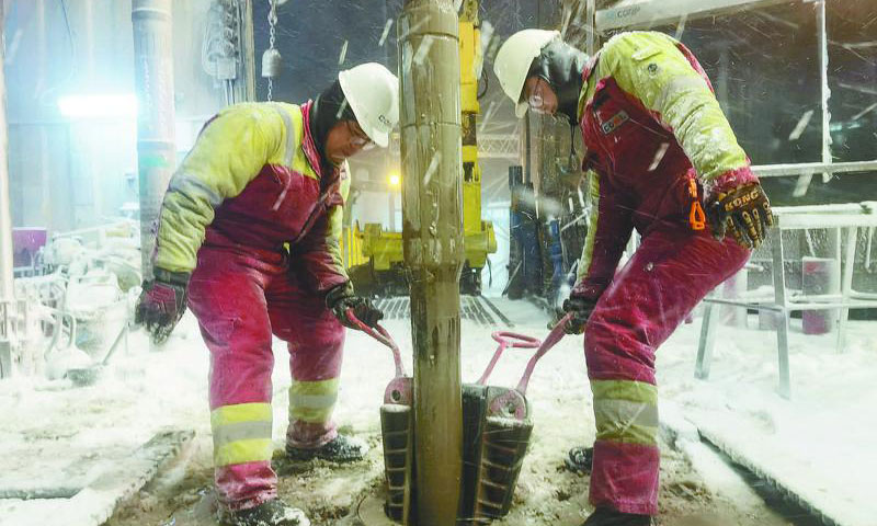 中國海油員工頂風冒雪堅守一線，做好設備防凍、管線防堵和場地防滑工作，確保惡劣天氣下鉆井生產安全、有序、平穩運行，全力保障能源供應。圖為在起下鉆作業中，兩名鉆工冒著風雪合力進行坐卡瓦操作。