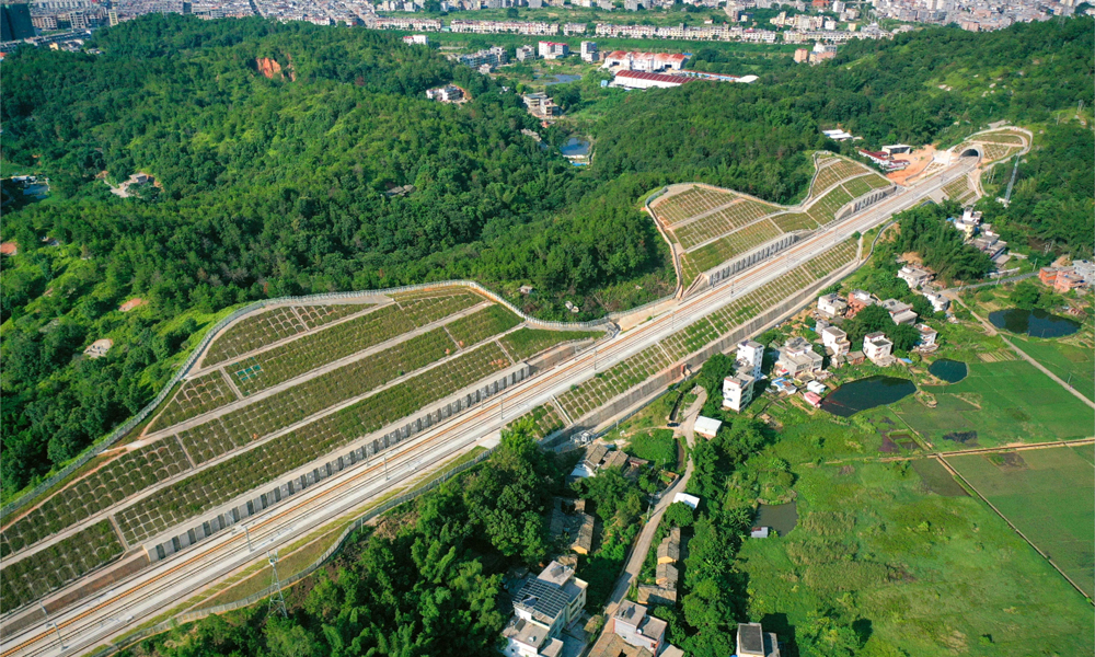 開工建設以來，中國鐵建各參建單位克服地質條件復雜、特殊結構多、山區氣候多變等諸多難題，保質保量完成了建設任務。全長7377米的下黃田隧道是全線最長隧道，其最大埋深290米，穿越山區多條地質破碎帶、巖溶強烈發育帶，地下水豐富。施工中，中鐵二十五局建設團隊采取長隧短打、斜井開挖的方式，多點施工、協同作業，并采用3D全息掃描分析等新型工裝工藝和智能化建造技術，為隧道貫通提供了保障。圖為龍龍高鐵梅龍段路基航拍。